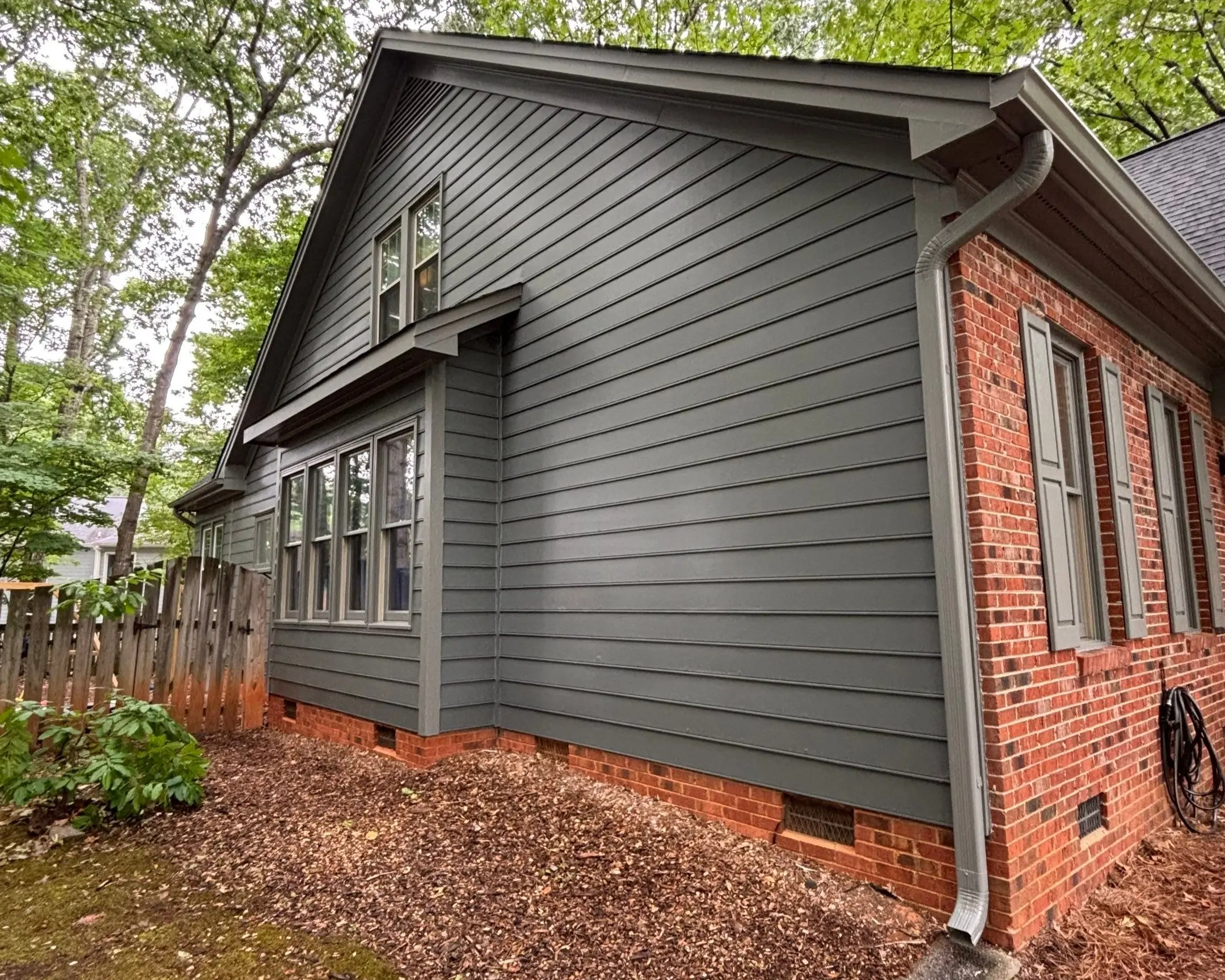 Exterior House Painting Gray Siding and Brick Combination Side view of a house with dark gray siding and red brick, showing new paint.