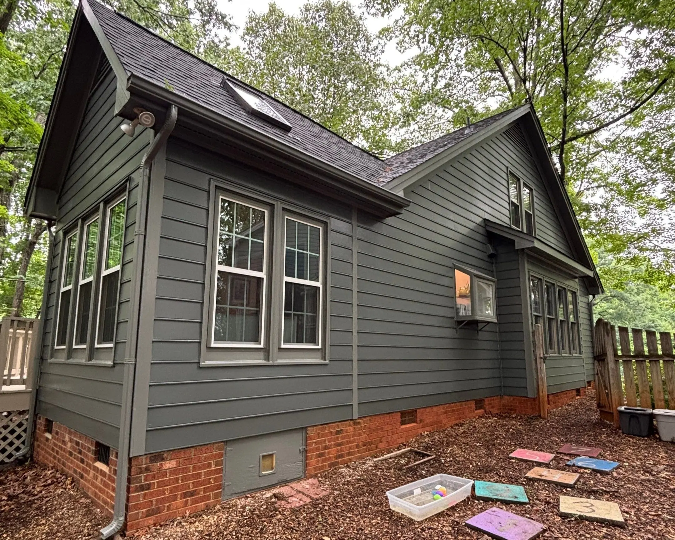 Residential Exterior Painting Gray Siding and White Windows A house exterior with dark gray siding, white windows, and a wooden fence.