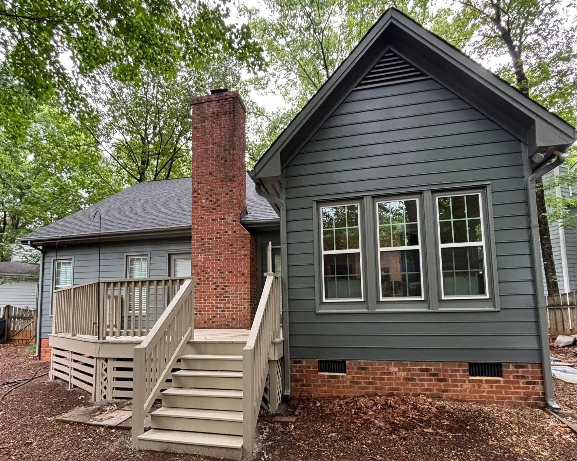 Backyard House Exterior Painting Gray Siding and Deck Side view of a house with dark gray siding and red brick, showing new paint.