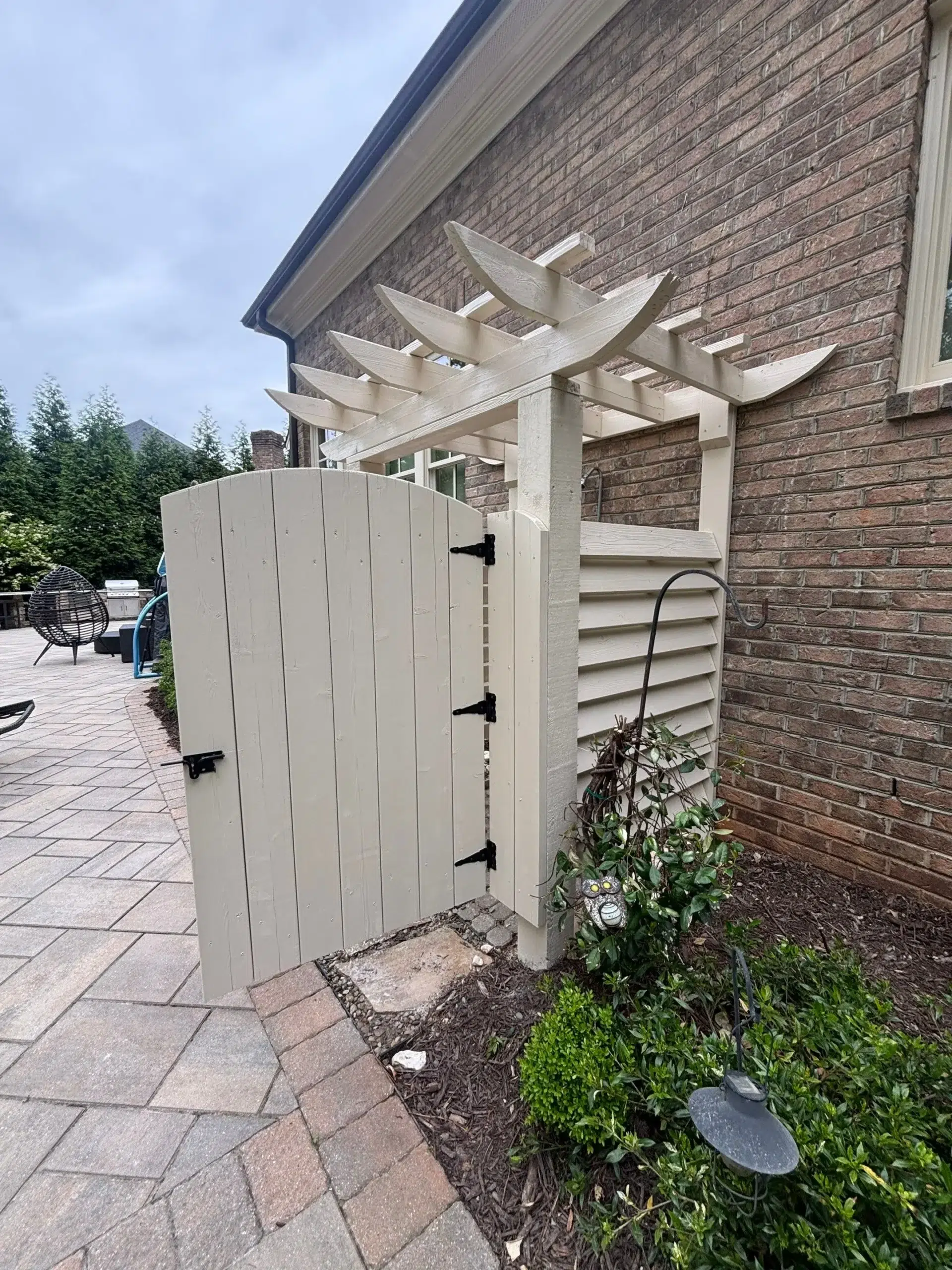 Painted Wooden Gate and Pergola Light Beige Exterior A newly painted light beige wooden gate and pergola structure next to a brick house.