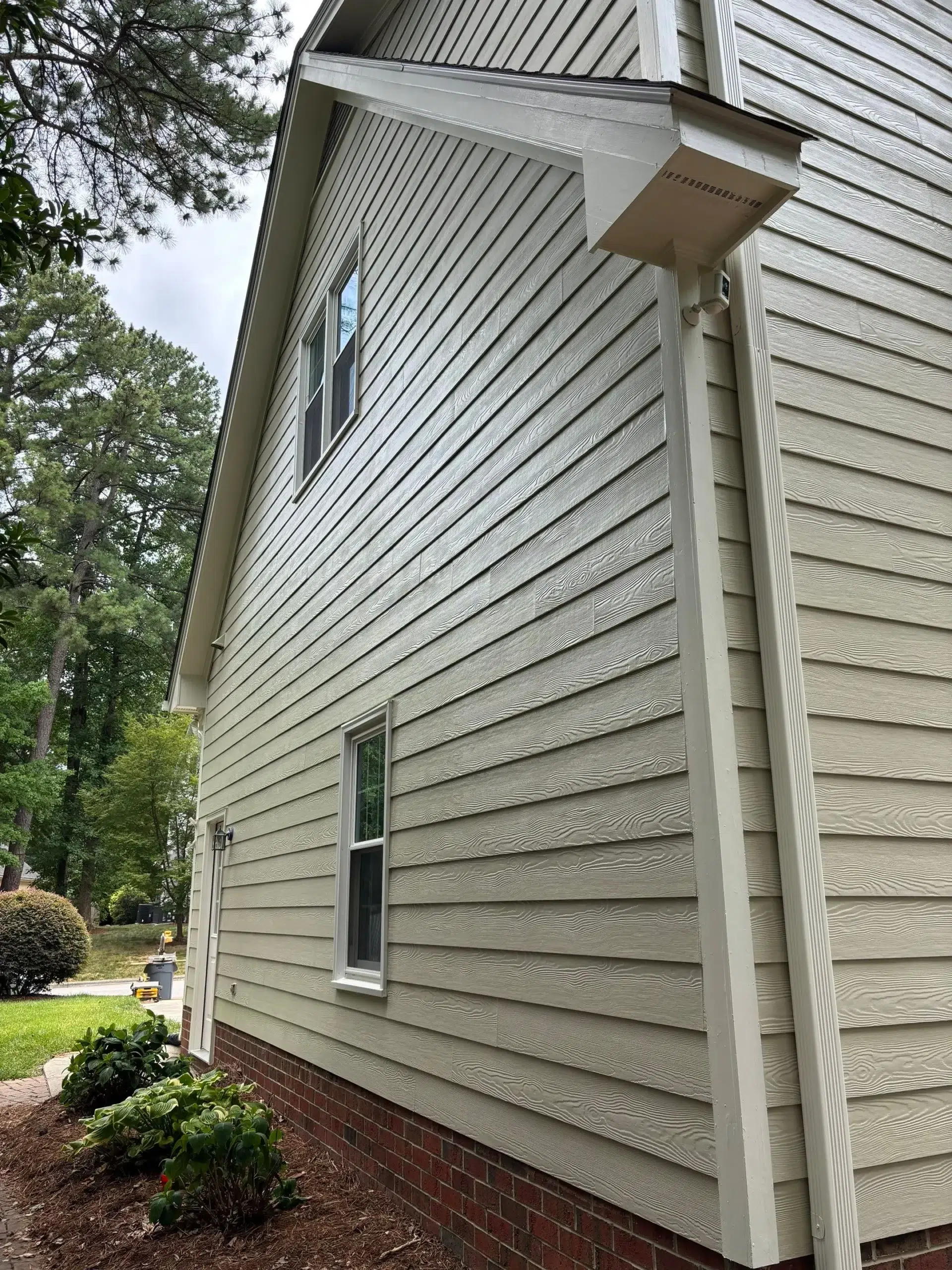 Professional Exterior House Painting for Siding and Trim Side view of a house with freshly painted light green siding and crisp white trim, surrounded by landscaping.