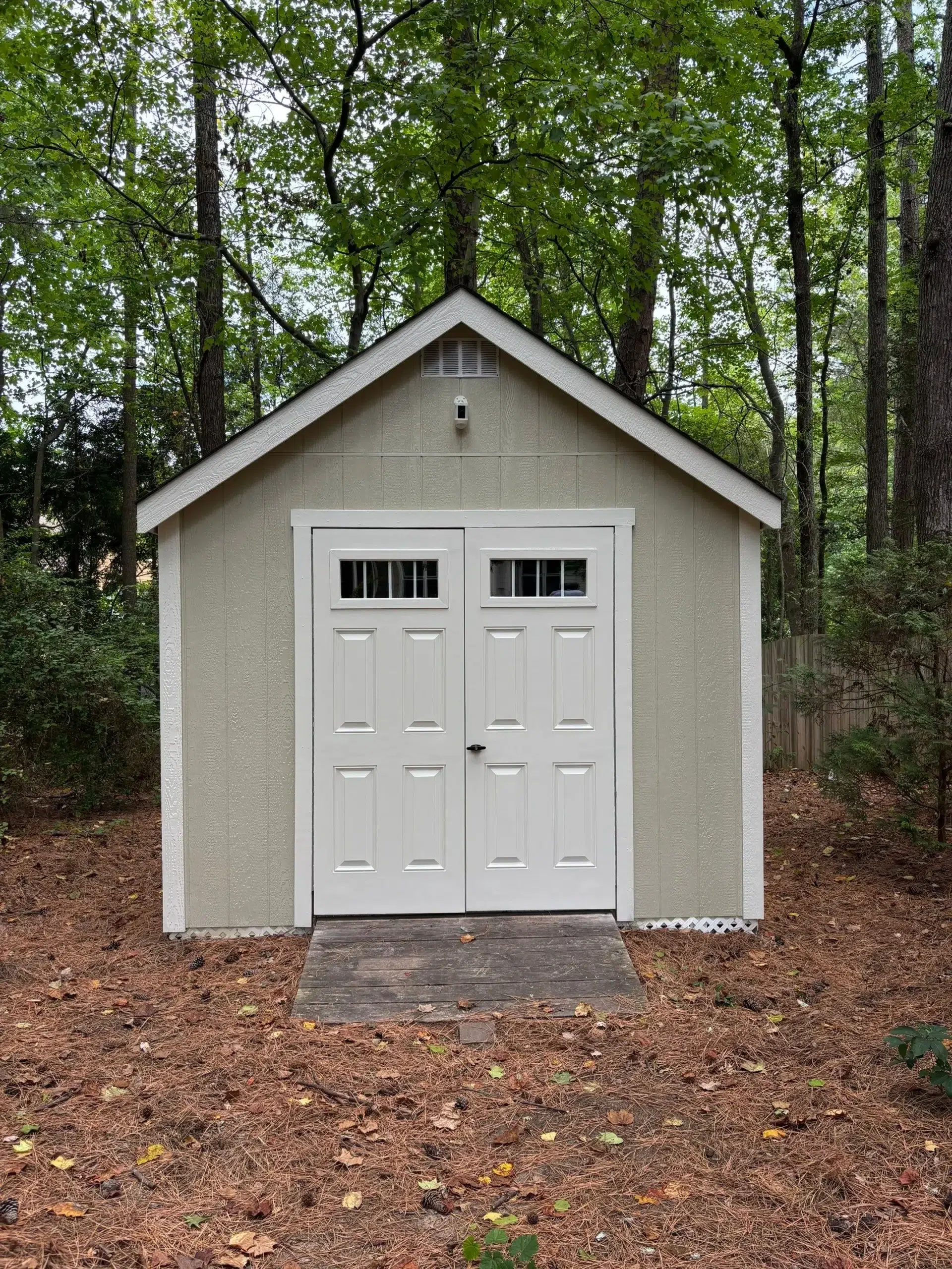 Expert Shed Painting and Exterior Structure Finishing A freshly painted light green shed with crisp white trim and double doors, nestled in a wooded backyard.