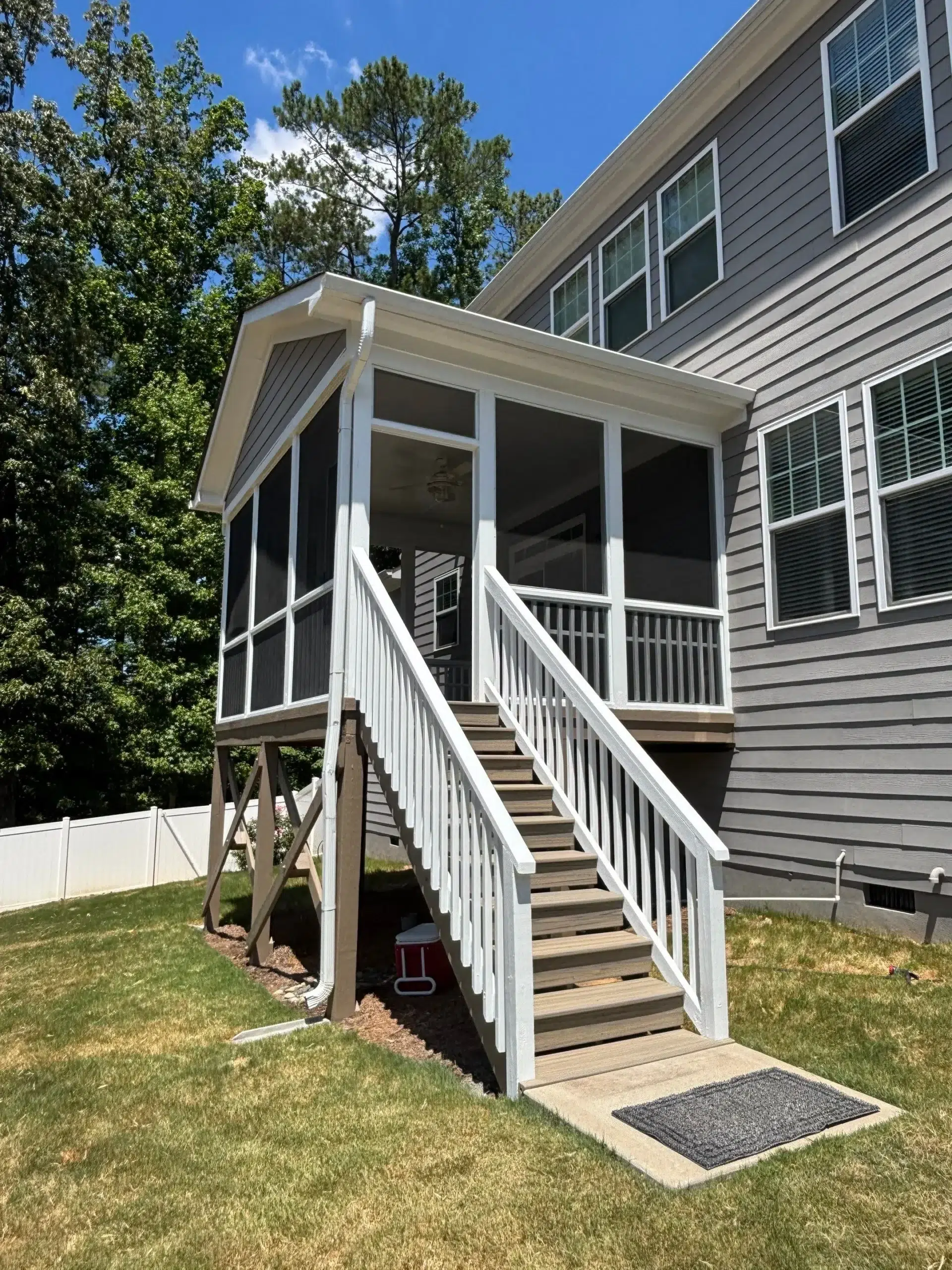 Expert Exterior House Painting and Screened Porch Finishing A modern house exterior with gray siding and a newly painted white screened porch leading to the lawn.