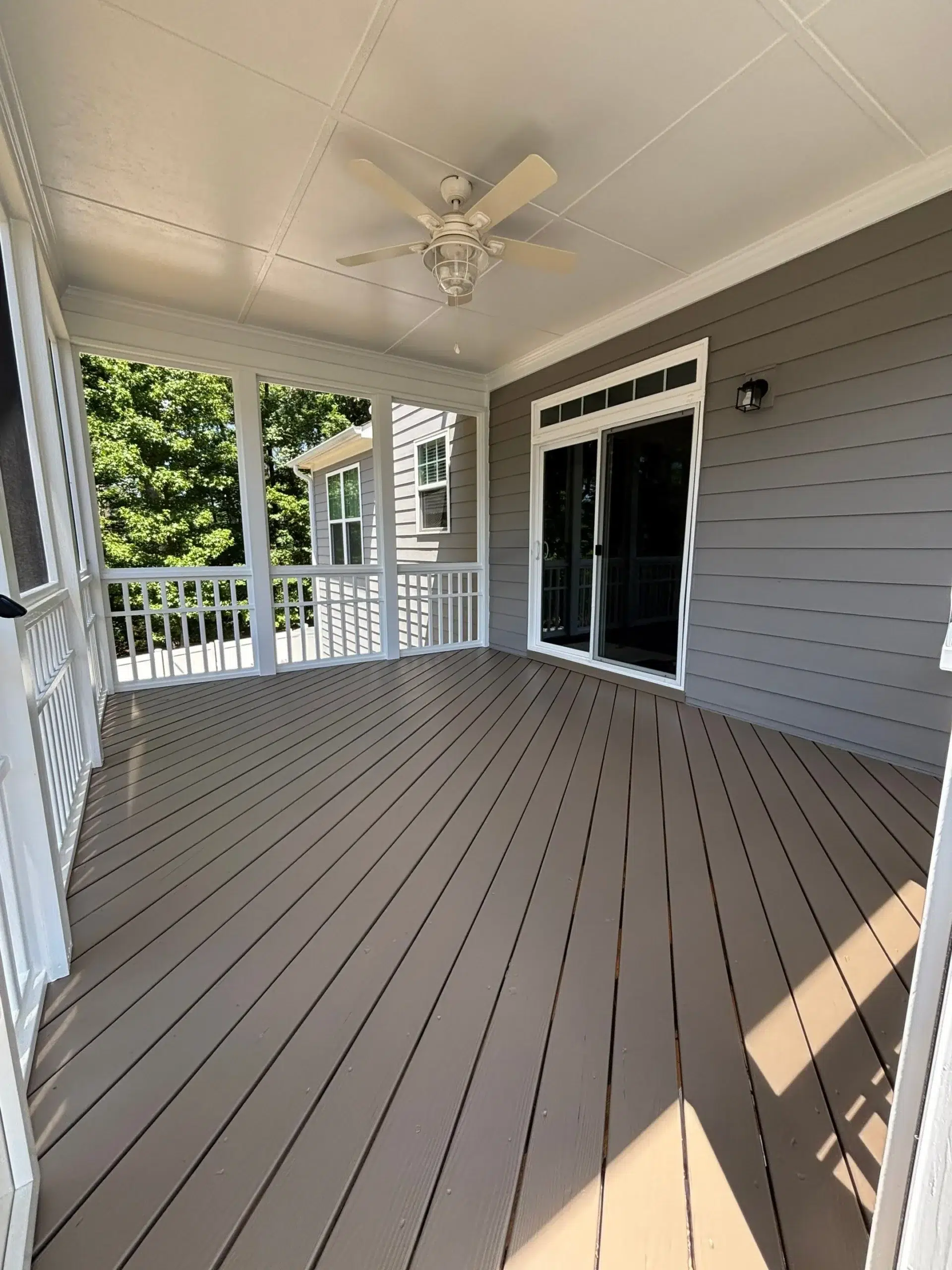 Professional Screened Porch Deck and Railing Painting A freshly painted screened porch interior featuring a brown deck floor, white railings, and a ceiling fan.