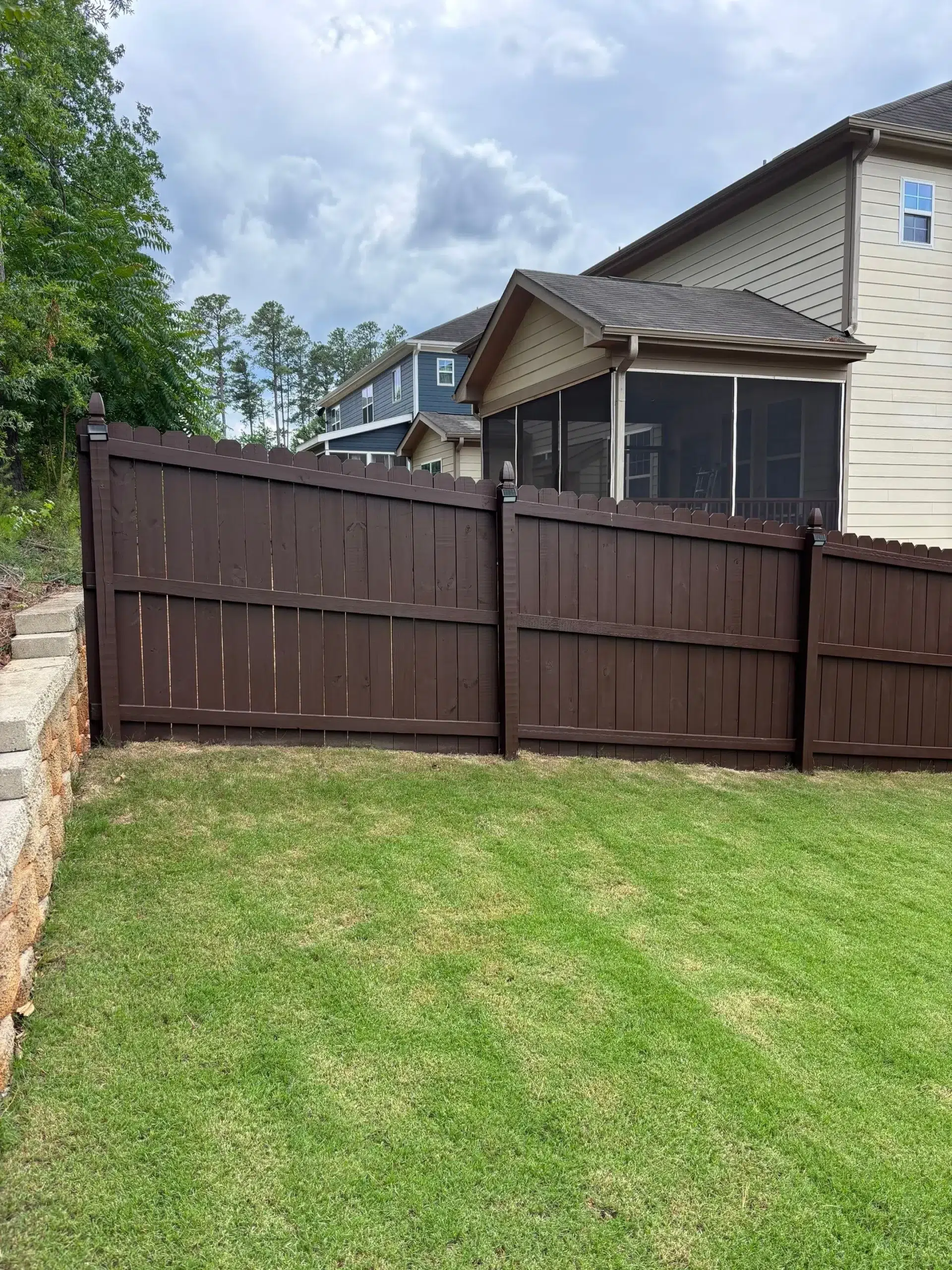 Quality Wood Fence Painting and Staining Services A long, newly painted dark brown wooden fence enclosing a green backyard, enhancing curb appeal.
