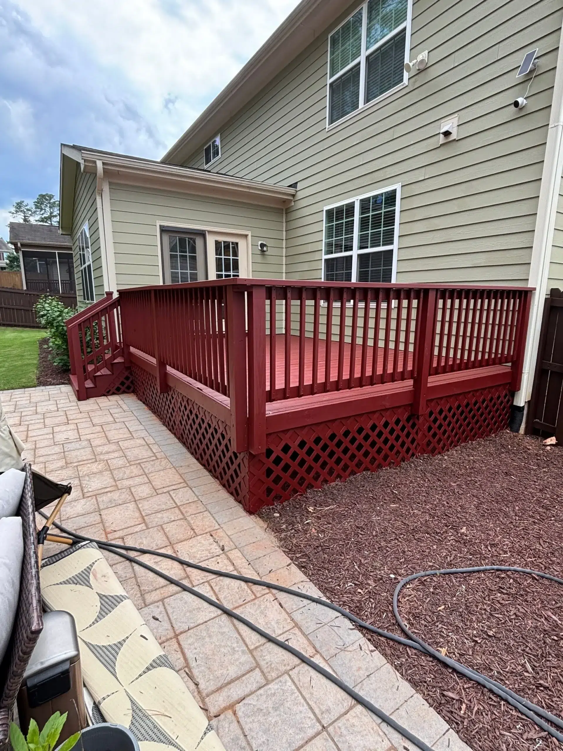 Professional Deck Painting and Staining Services A vibrant red painted wooden deck with lattice skirting and stairs next to a light green house.
