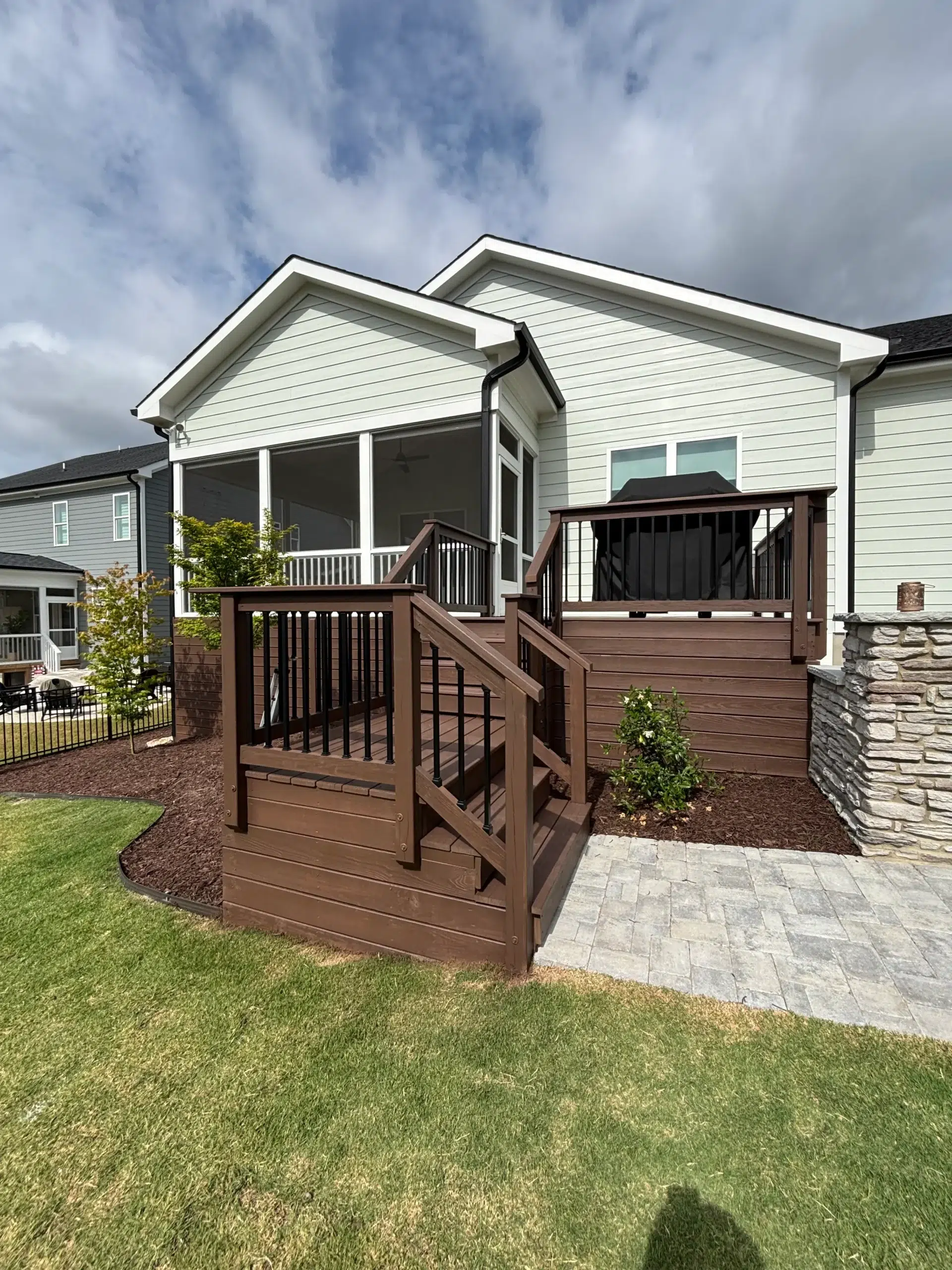 Expert Deck Staining and Exterior Home Painting A beautifully stained brown wooden deck with black railings and stairs leading to a screened porch.