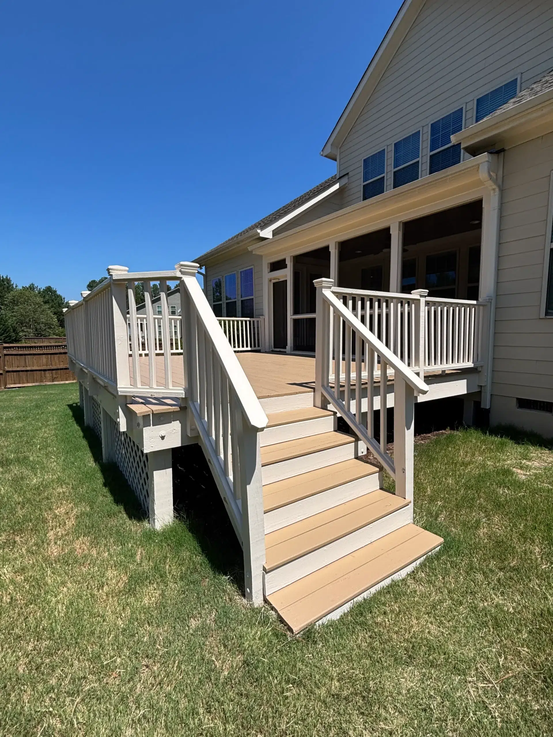 Expert Deck Painting and Staining Services for Residential Homes Newly painted light beige deck with white railings and steps leading to a green backyard.