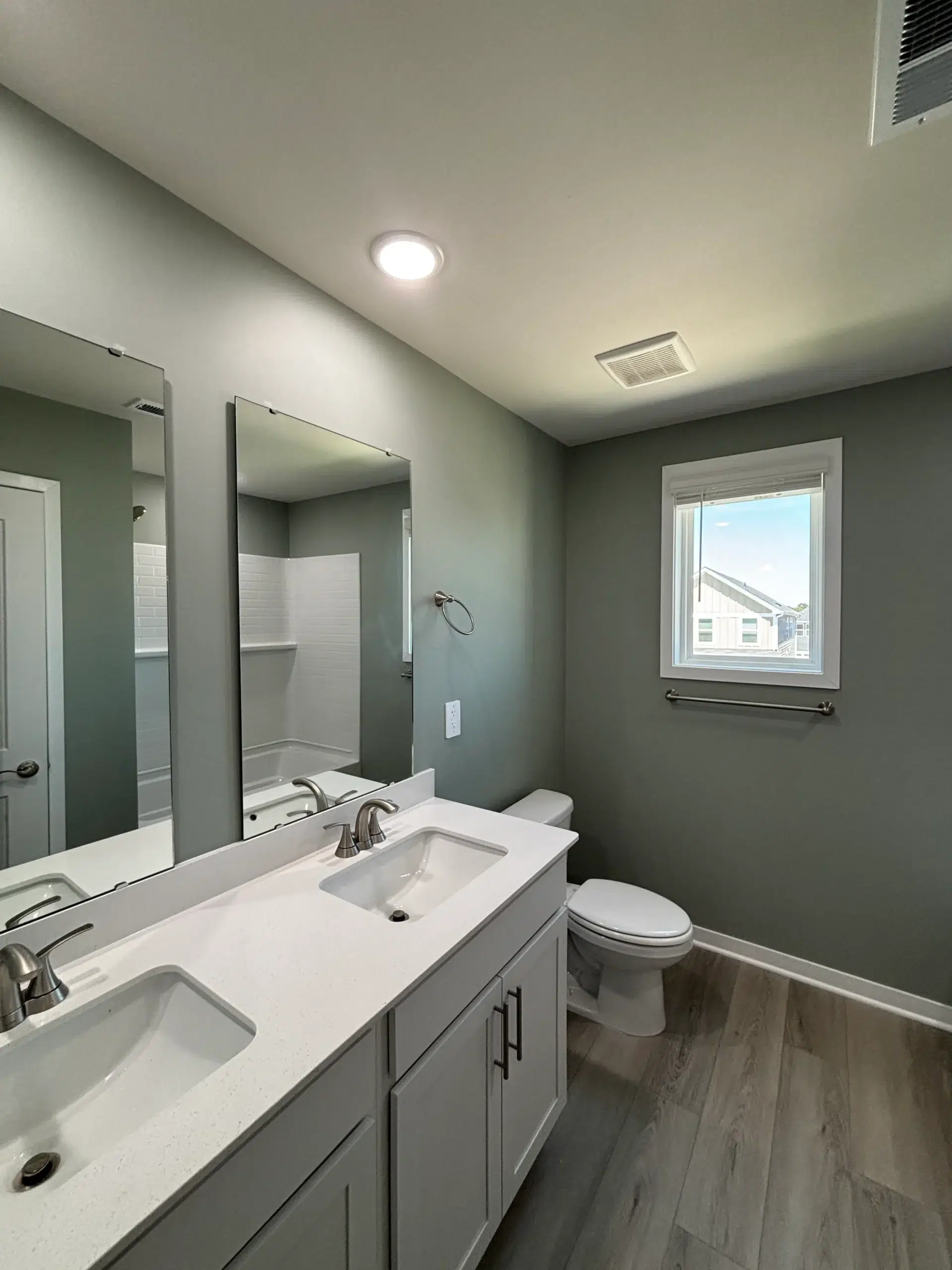 Fresh Light Green Bathroom Interior Painting Project A newly painted modern bathroom with light green walls, a double vanity, toilet, and window, ready for use.