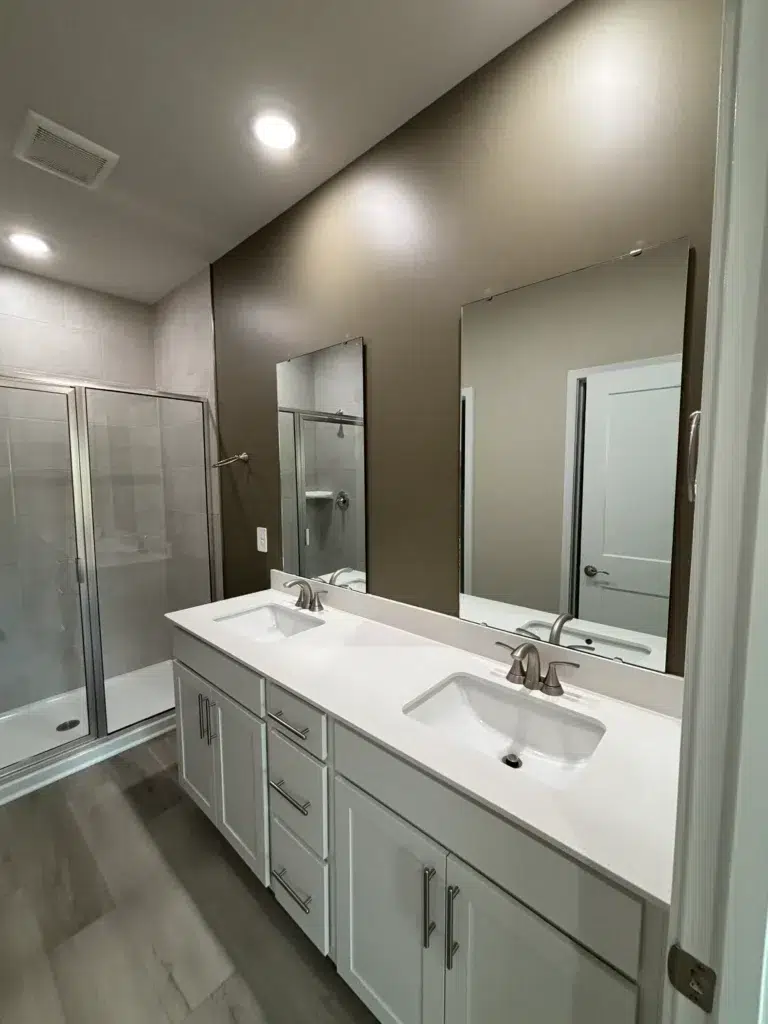 A contemporary bathroom with a dark brown accent wall, double vanity, and glass shower, showcasing fresh paint.