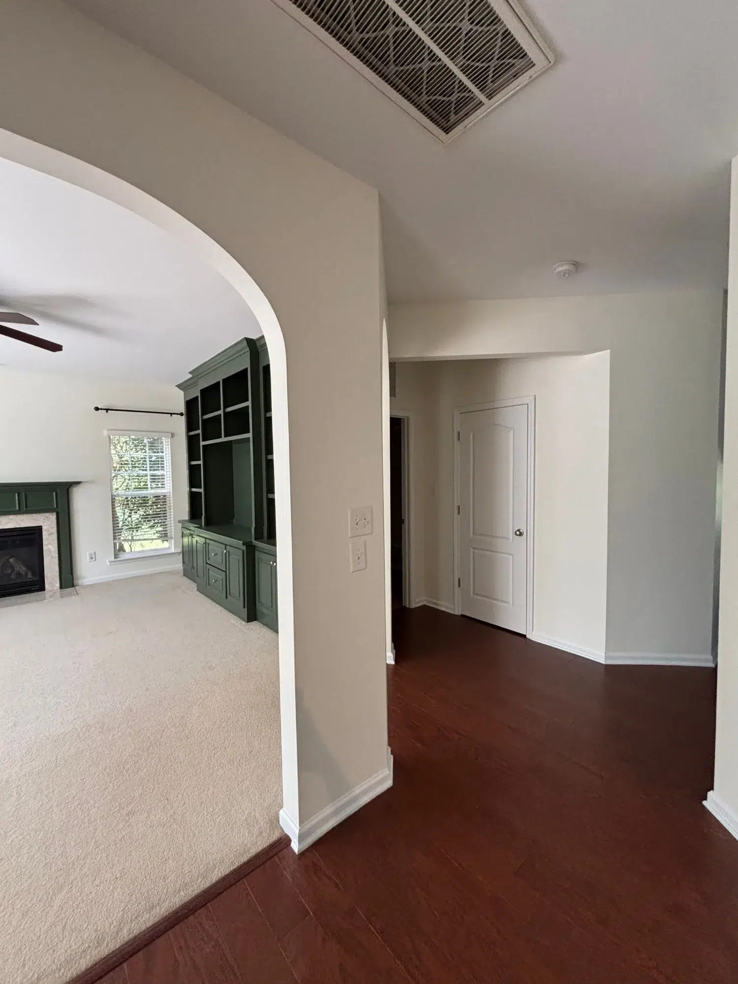 Cream And Taupe Interior Hallway Cream-painted hallway with taupe accent wall, dark hardwood flooring, white-trimmed doors, and arched entry to living room