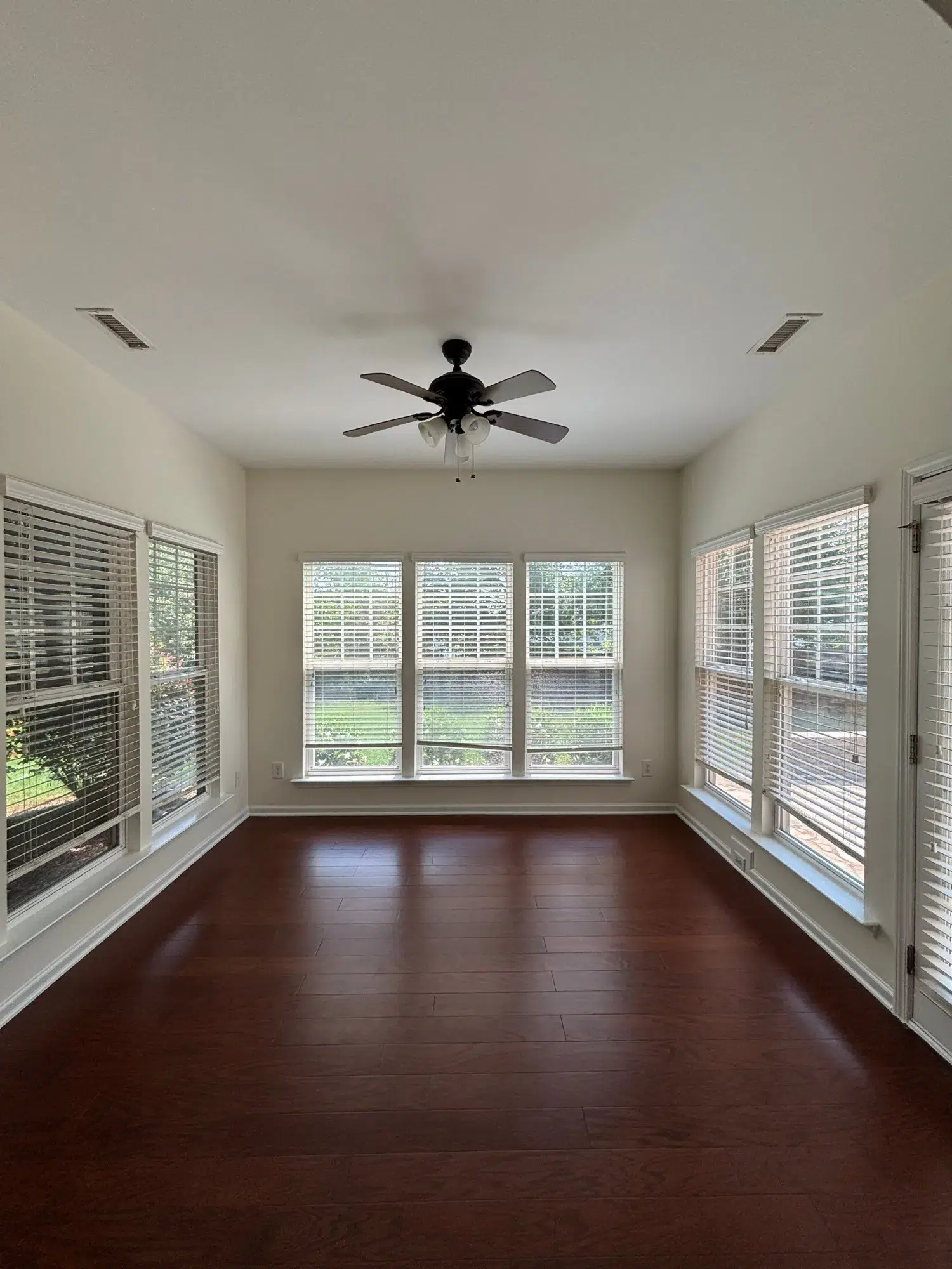 Cream Interior Room Hardwood Flooring Cream-painted interior room with dark hardwood flooring, white-trimmed windows, black ceiling fan, and recessed lighting