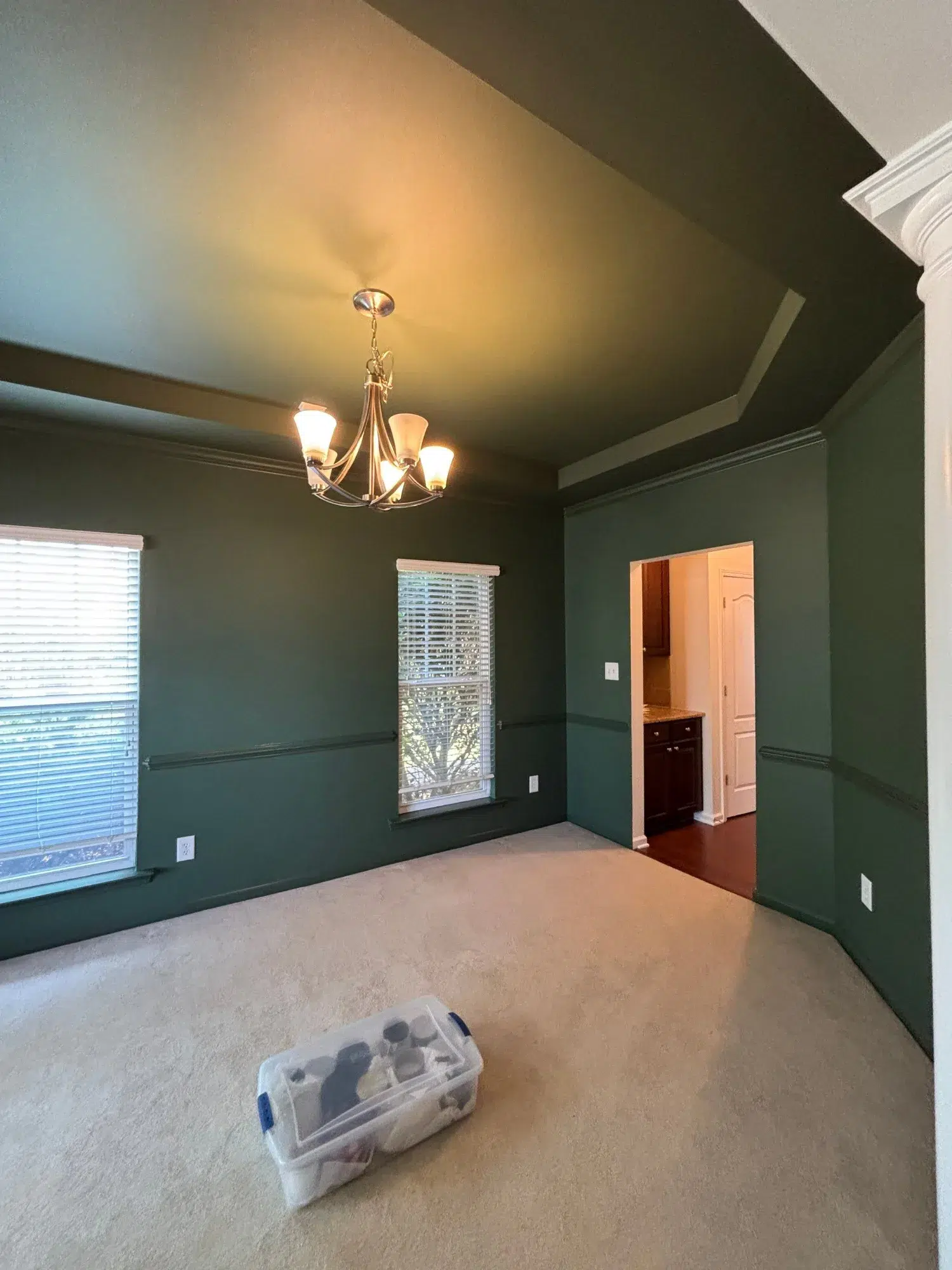 Forest Green Interior Painted Room Forest green painted walls with white crown molding, tan carpet, brass chandelier, and windows in residential interior